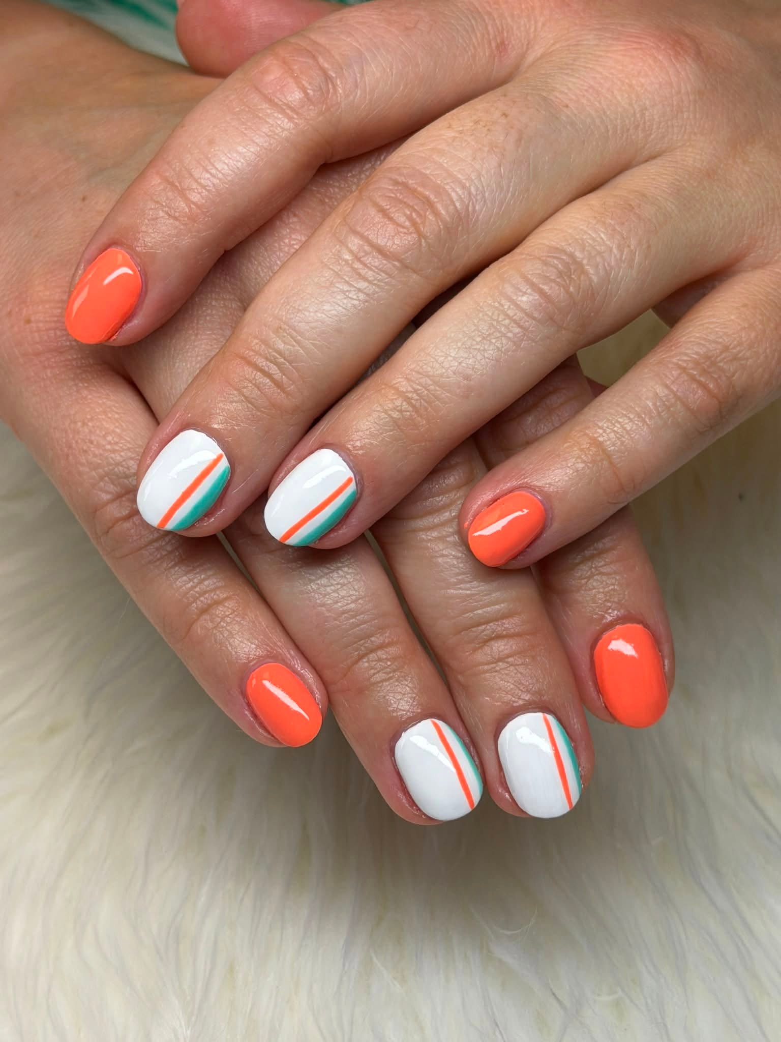 Orange nails paired with white nails featuring orange and teal stripe nail art