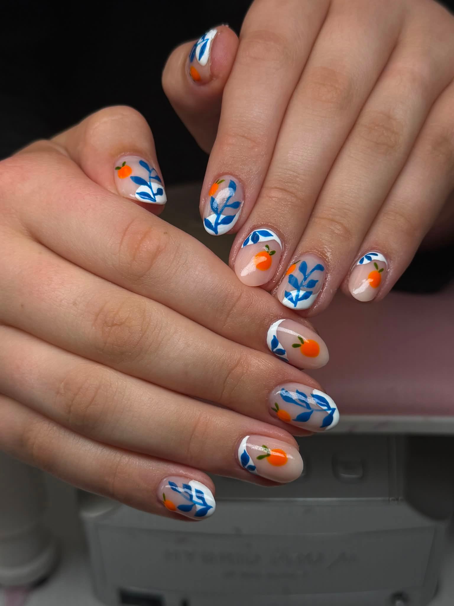 Nude French manicure with blue floral and orange fruit art